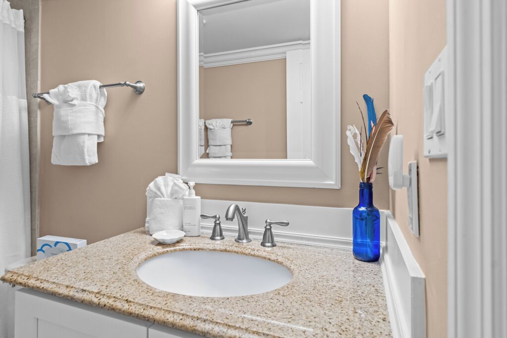 A bathroom with a beige wall, a white sink, and a blue vase with decorative items.