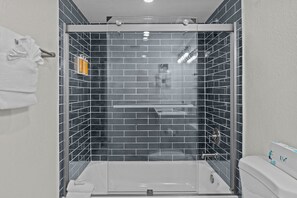 A bathroom with a glass-enclosed shower, a white bathtub, and a toilet.