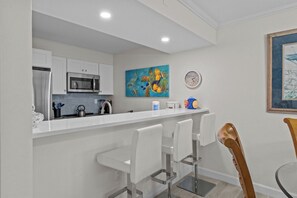 A modern kitchen with white cabinets, stainless steel appliances, and a bar area with white bar stools.
