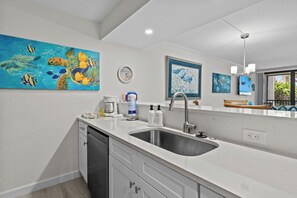 A modern kitchen with white cabinetry, a stainless steel sink, and a large painting of marine life.