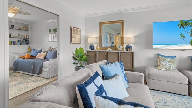 A living room with a sofa, armchairs, a coffee table, a bookshelf, a mirror, and a painting of a beach.