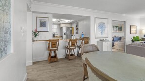 A modern kitchen with white cabinets, a dining area with a large table and chairs, and a living room with a sofa and a coffee table.