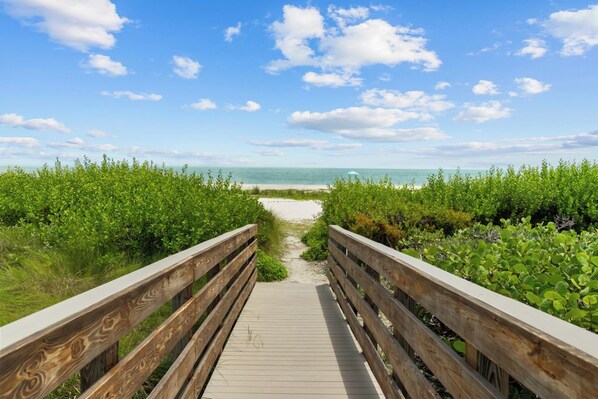 A wooden boardwalk leading to a beach with a clear sky.