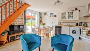 Une cuisine moderne avec des meubles blancs, un lave-vaisselle et un lave-linge. On y trouve un coin repas avec une table et des chaises, ainsi qu’un téléviseur posé sur un meuble en bois.