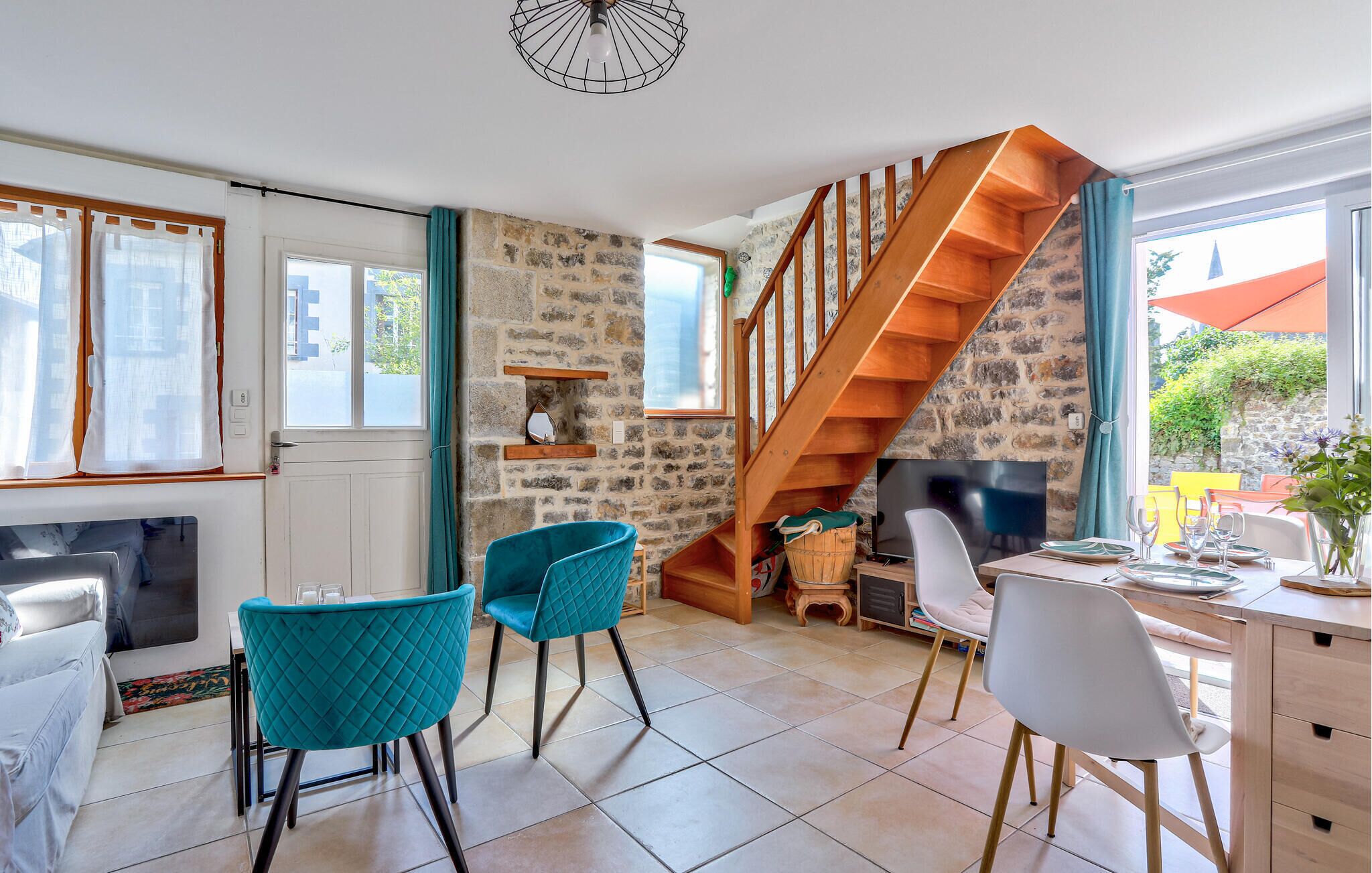 A modern kitchen with a stone wall, wooden staircase, and teal chairs.