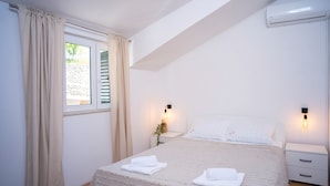 A bedroom with a bed, two bedside tables, a nightstand, a window with curtains, and an air conditioning unit.
