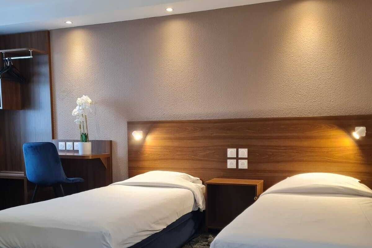 A hotel room with two beds, a desk, a chair, and a small table with a vase of flowers.