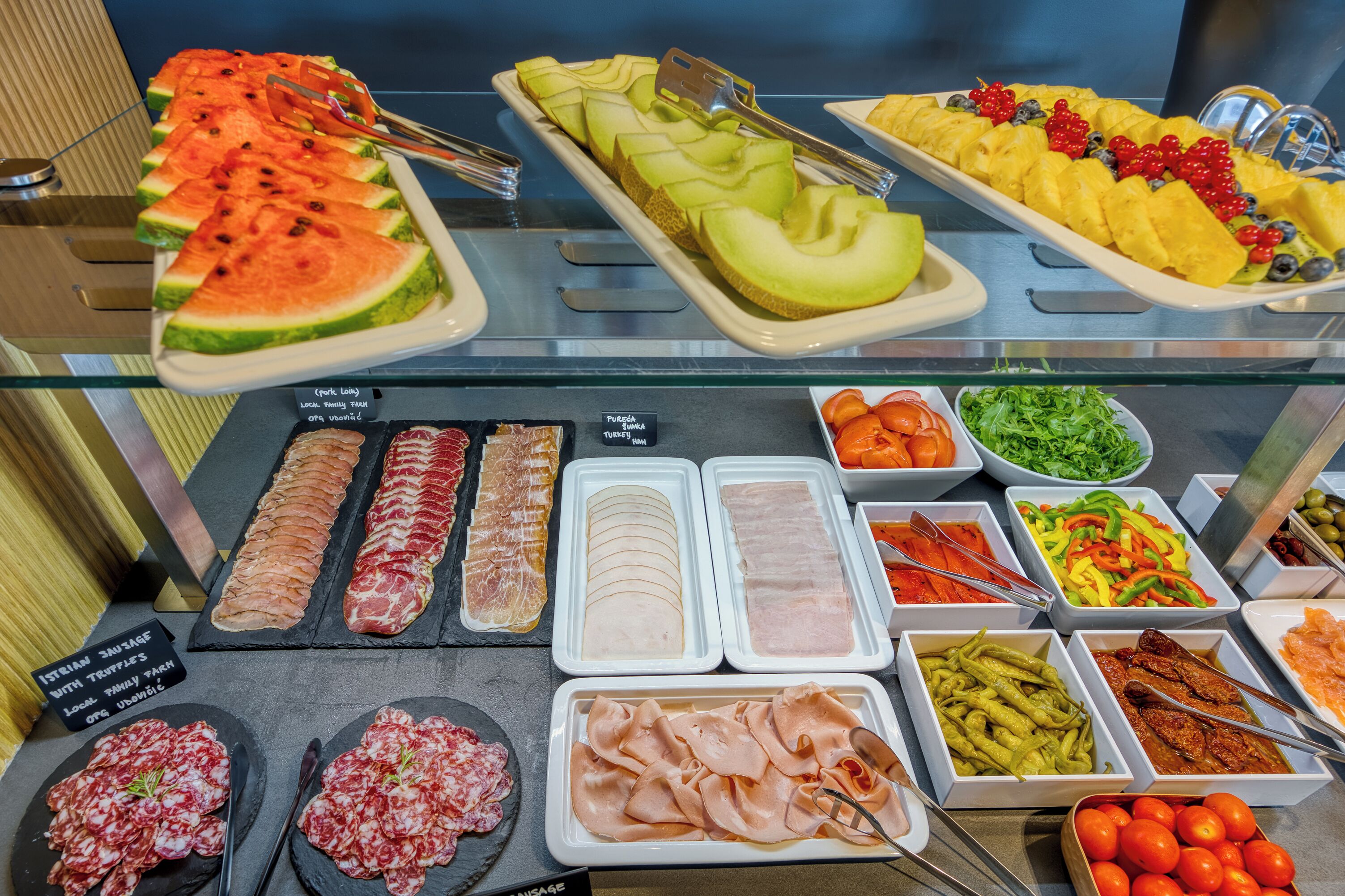 A buffet with various food options including sliced watermelon, cantaloupe, and a selection of meats and cheeses.