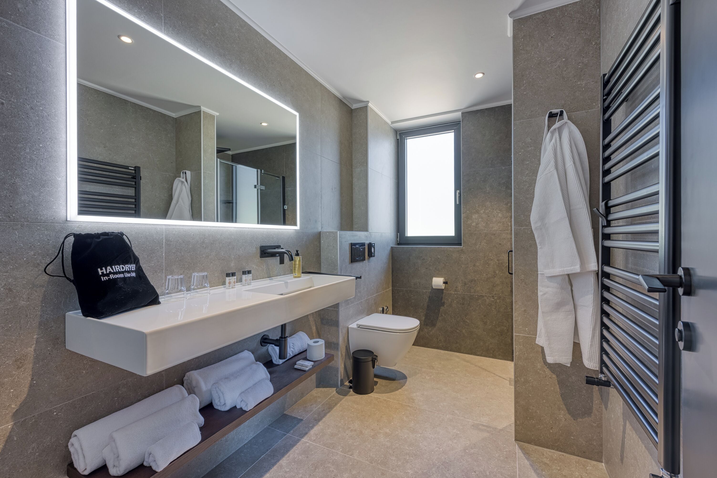 Une salle de bain moderne avec un grand miroir, un lavabo blanc, des toilettes et un porte-serviettes.