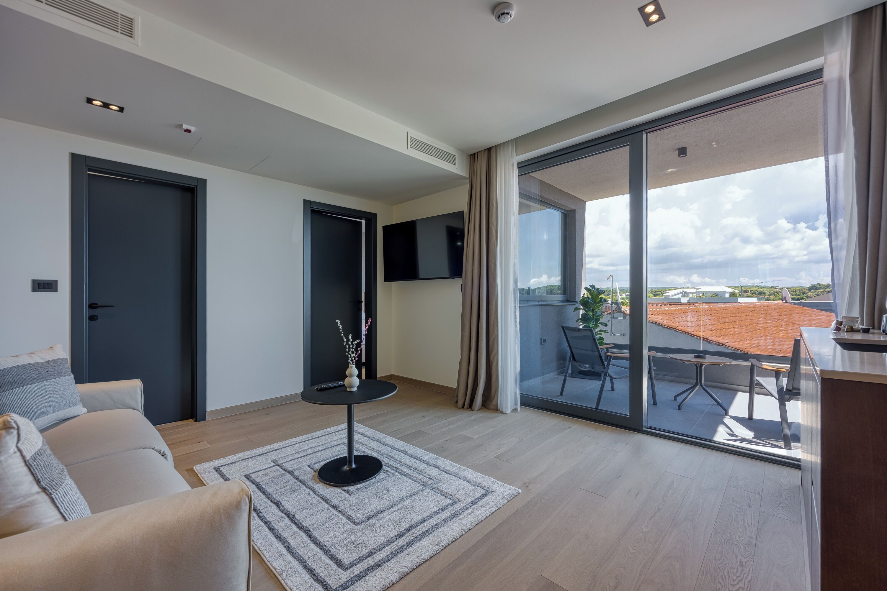 A modern living room with a sofa, a small table with a vase, and a large sliding glass door leading to an outdoor area with a table and chairs.