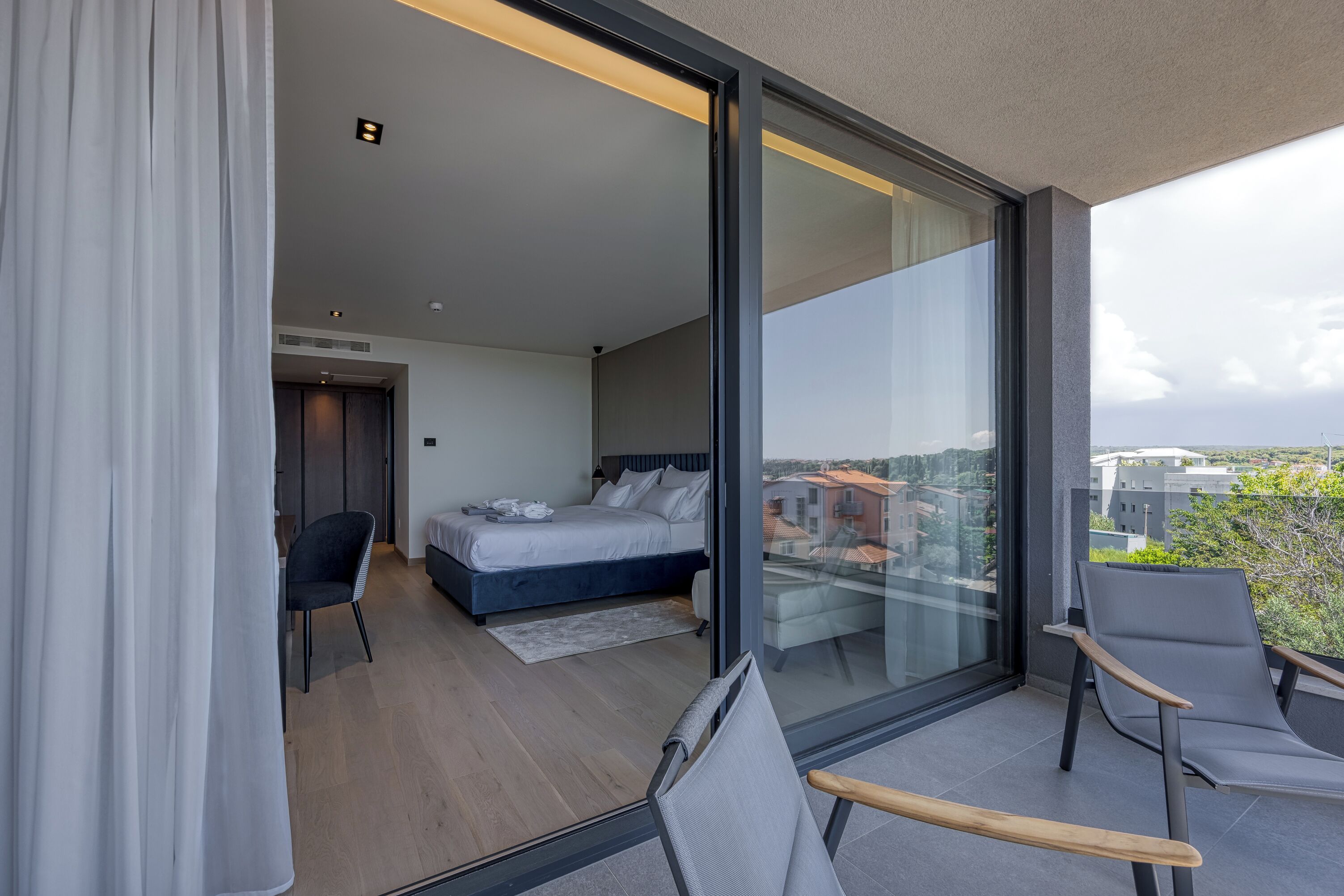 Un dormitorio moderno con una cama grande, un escritorio y una silla, y un balcón con vista a la ciudad.