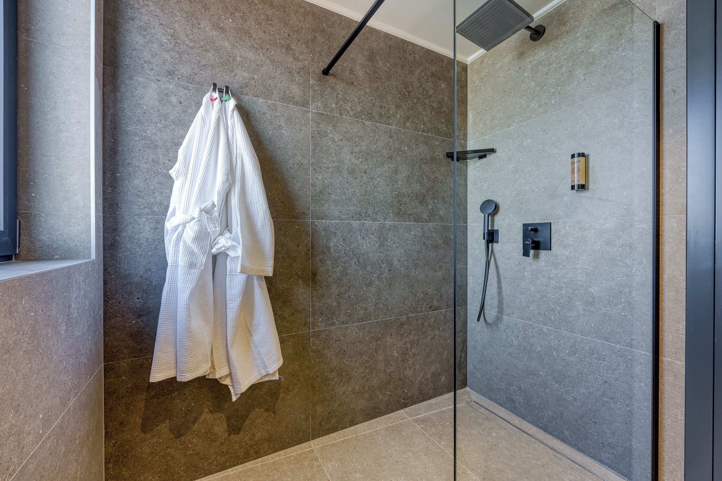 Um banheiro moderno com box de vidro, porta-toalhas com toalha branca e painel de controle fixado na parede.