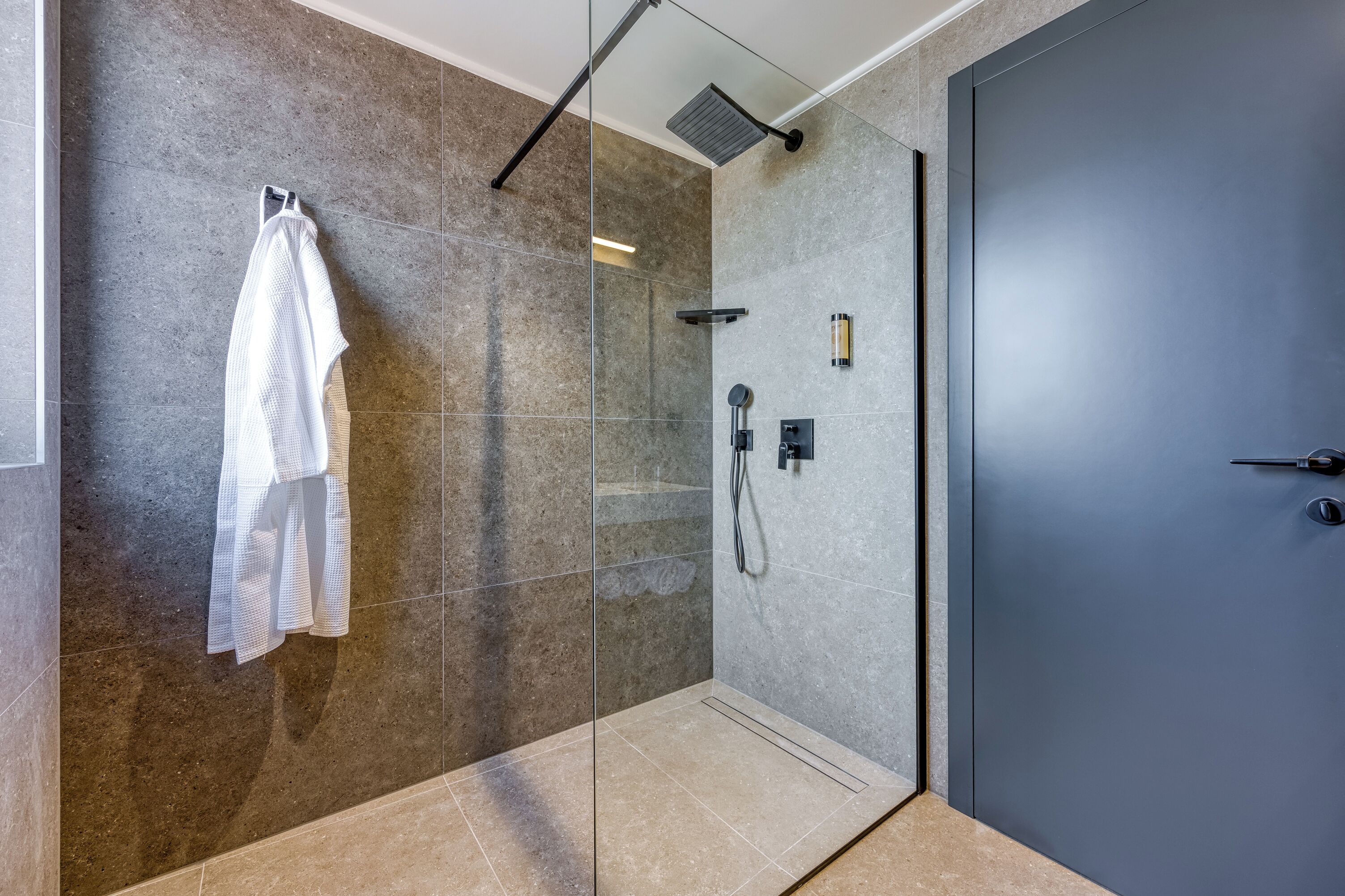 A modern bathroom with a glass shower enclosure, a towel rack, and a door.