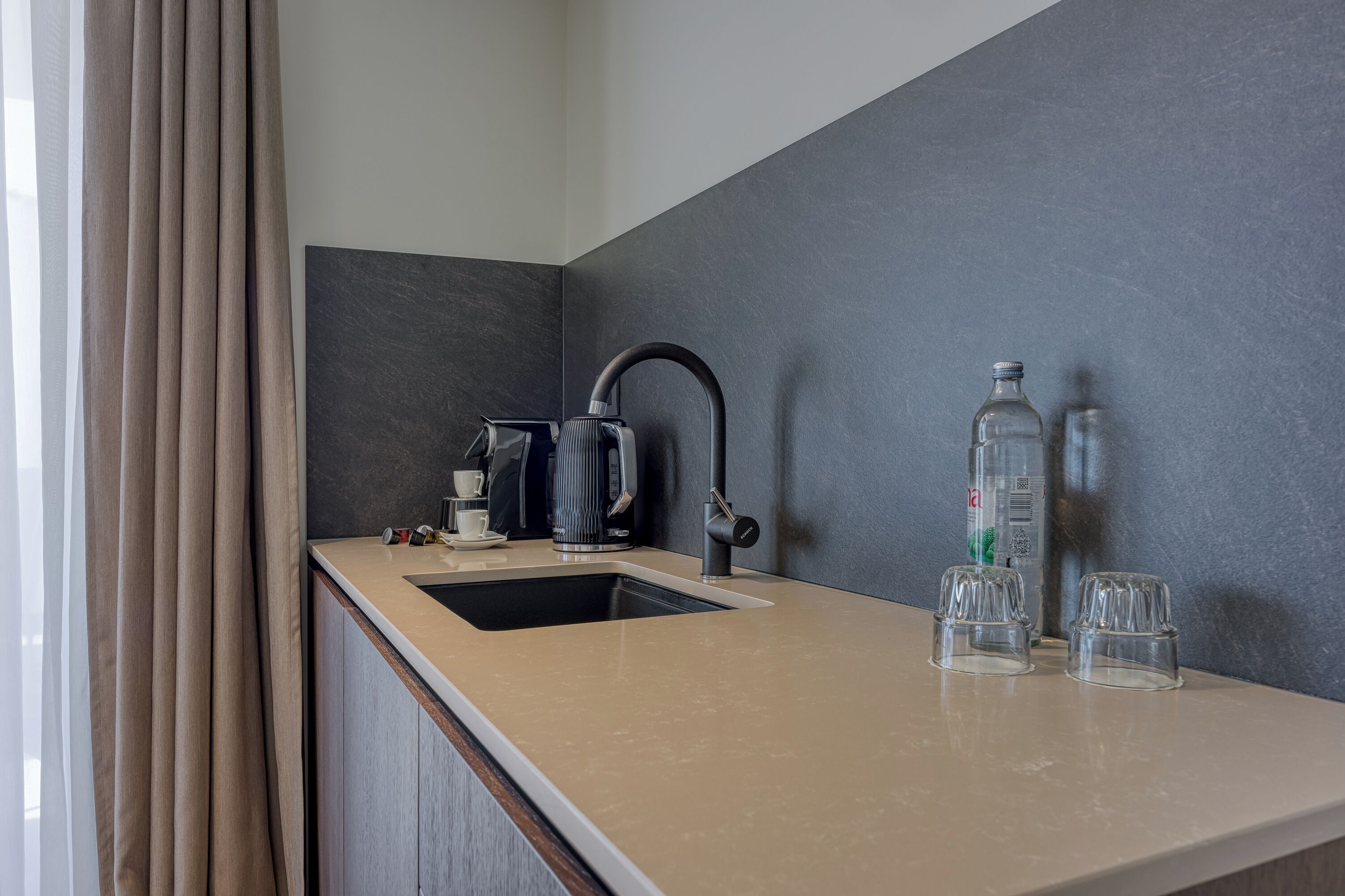A modern kitchen with a sink, a kettle, and two glasses on the counter.