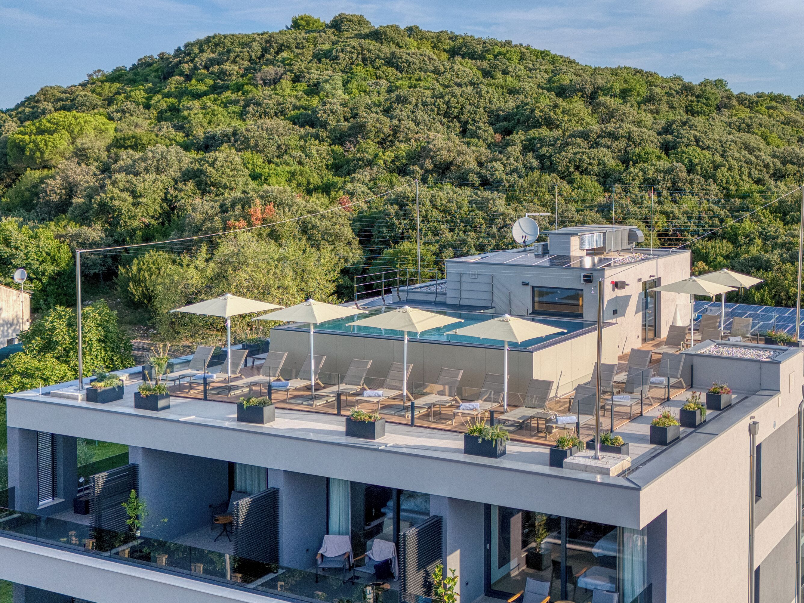A rooftop terrace with outdoor seating, a pool, and a view of a forested hill.