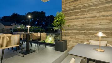 An outdoor patio area with tables and chairs, a potted plant, and a stone wall.