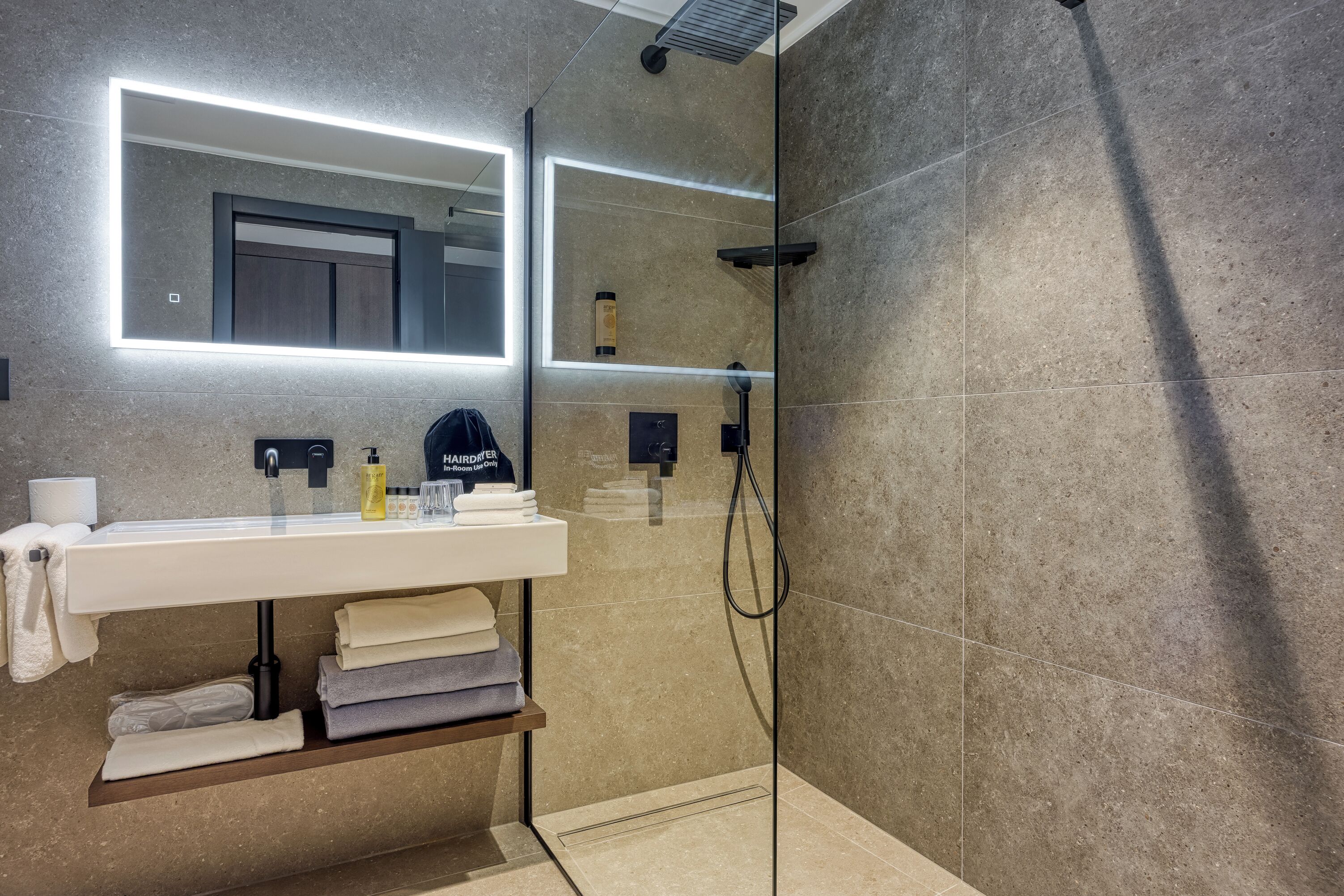 Un baño moderno con ducha envuelta en vidrio, tocador con espejo y toallas dobladas con esmero.