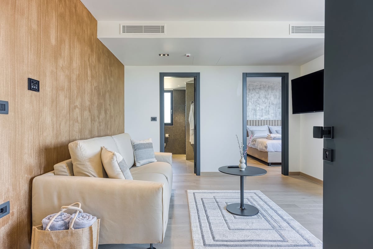 Ein modernes Hotelzimmer mit einem beigefarbenen Sofa, einem kleinen runden Tisch und einem an der Wand montierten Fernseher.