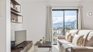 Ein modernes Wohnzimmer mit Flachbildfernseher, einer Couch, einem Couchtisch und einem Balkon mit Blick auf die Stadt.