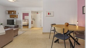 Ett modernt hotellrum med en soffa, en TV, ett matbord med stolar och en rosa accentvägg.