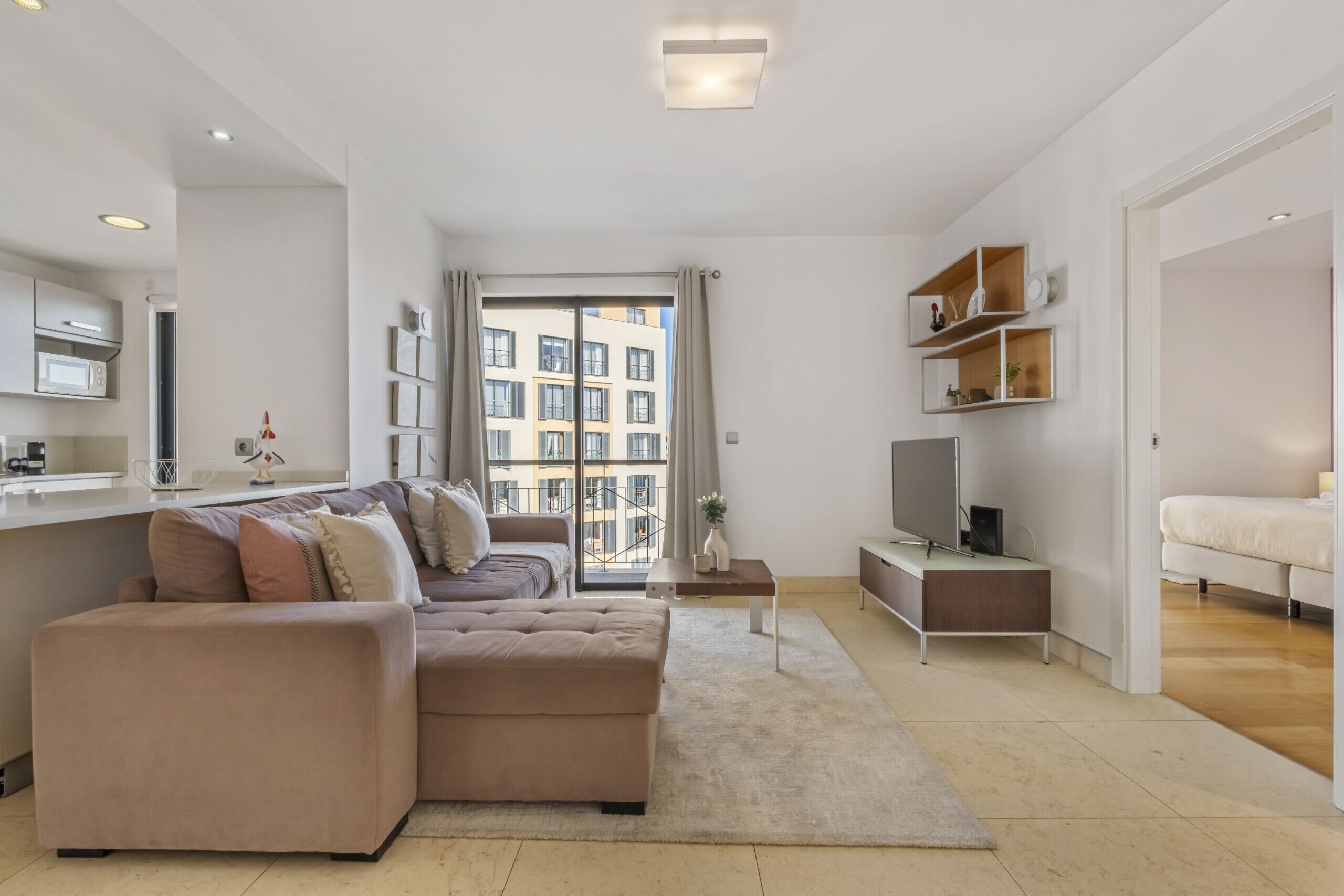 A modern living room with a beige sectional sofa, a flat-screen TV, and a dining area with a white table and chairs.