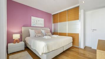A modern bedroom with a large bed, a nightstand with a lamp, and a wooden wardrobe.