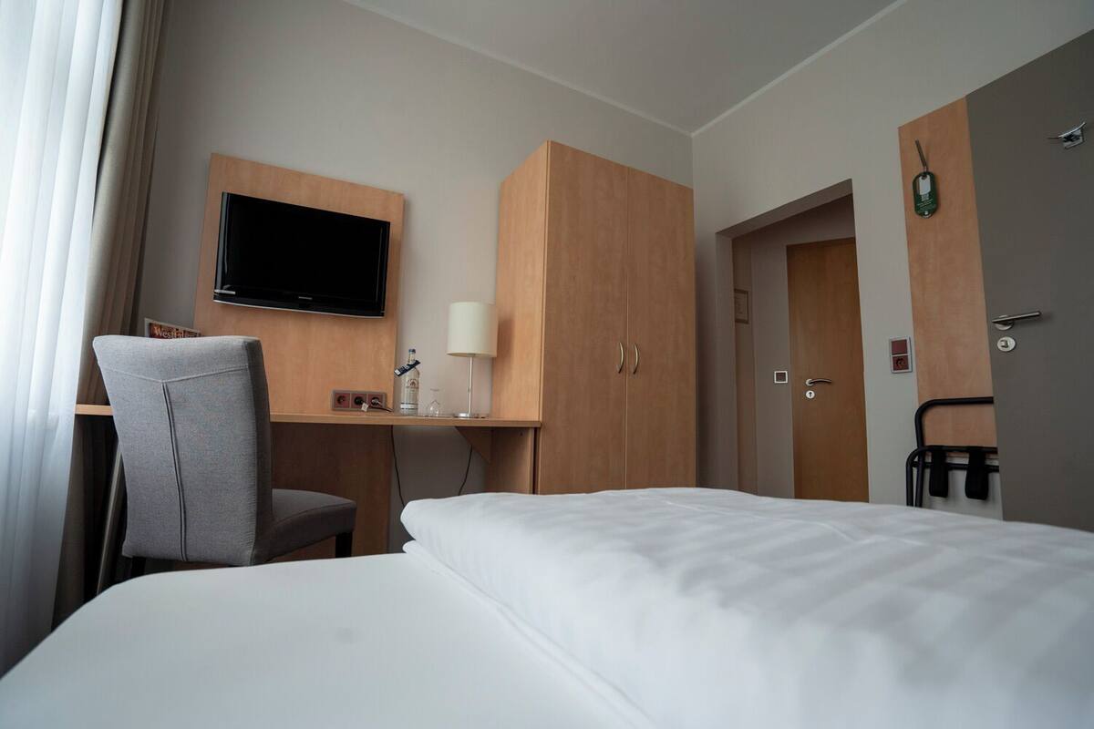 Hotellihuone, jossa on sänky, työpöytä tuolilla, televisio ja vaatekaappi.