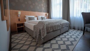 Una habitación de hotel con una cama grande, una mesita de noche, una silla y una alfombra estampada.