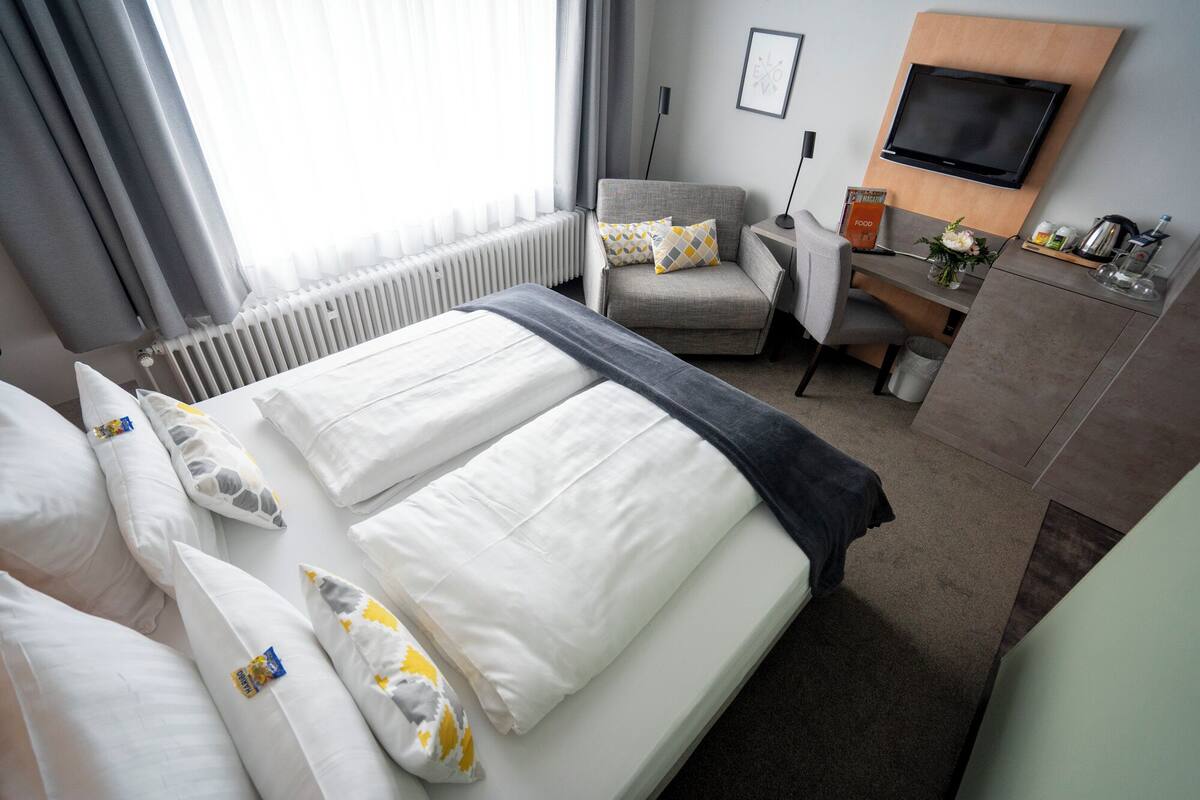 Hotellihuone, jossa on sänky, työpöytä, tuoli, televisio ja patteri.