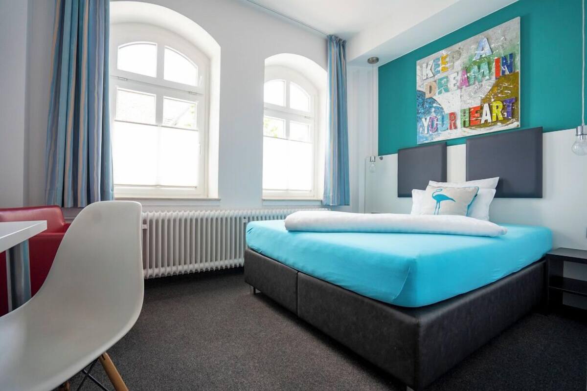 Hotellihuone, jossa on sänky, tuoli, pöytä ja ikkuna, jossa on verhot.