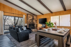 A cozy living room with a stone fireplace, a black sofa, and a dining table set for six.