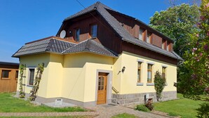 Uma casa de dois andares com telhado inclinado, fachada amarela e um caminho de tijolos que leva à entrada.