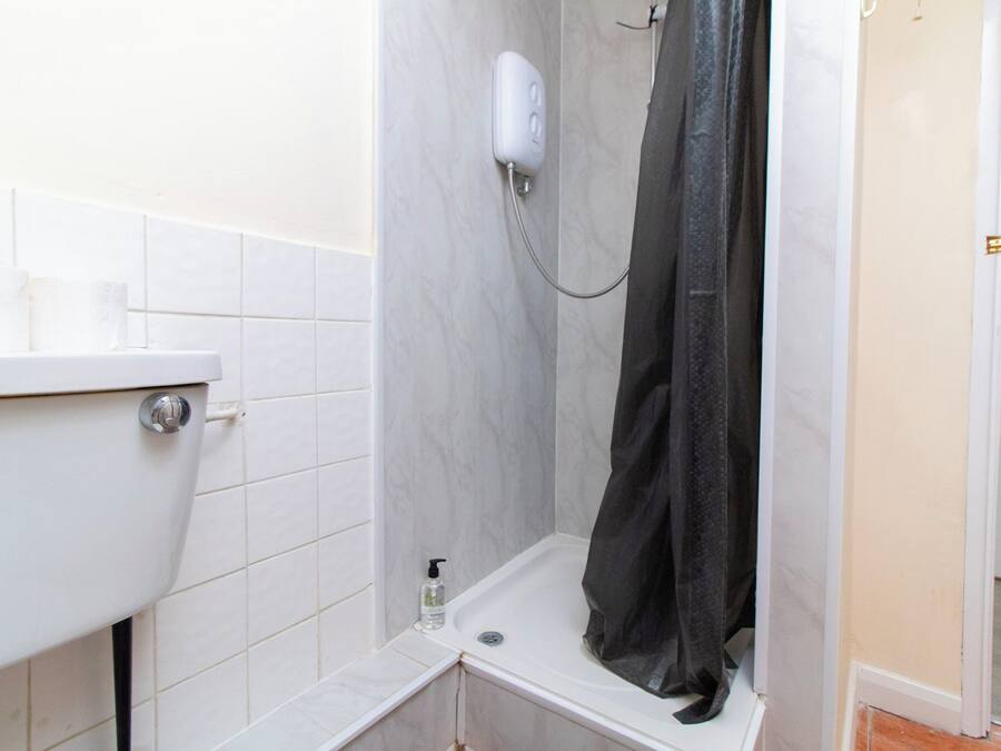Un baño con un lavabo blanco, una ducha con cortina negra y un inodoro blanco.