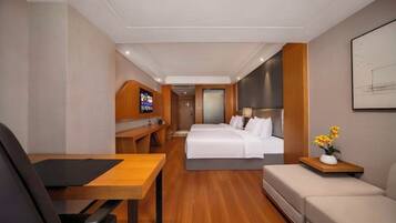 A hotel room with a bed, a desk, a chair, a sofa, and a TV.