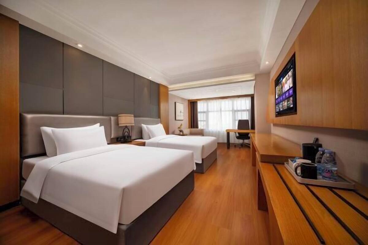 Ett hotellrum med två sängar, ett skrivbord, en stol och en tv på väggen.