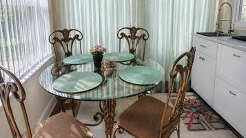 A dining area with a round glass table, four chairs, a cabinet, and a window with curtains.