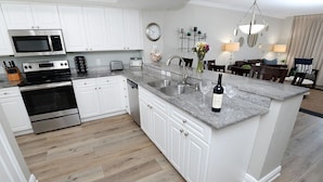 A modern kitchen with white cabinets, stainless steel appliances, a granite countertop, and a dining area with a chandelier.