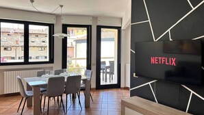 A modern living room with a dining area, large windows, and a TV screen displaying "NETFLIX". - Bergamo Center - Quarenghi House (Bergamo)