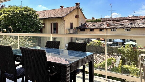 A balcony with a glass table and wicker chairs, overlooking a residential area with tiled roofs and greenery. - Bergamo Center - Quarenghi House (Bergamo)