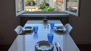 A dining table with plates, glasses, and cutlery set up in a room with a window overlooking a cityscape.