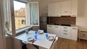 A compact kitchen with white cabinets, a dining table set for two, and a view of buildings through a window.