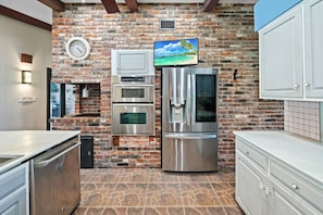 Enjoy cooking in this well-equipped kitchen with a stainless steel refrigerator, ovens, and a wall-mounted clock.