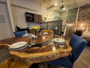 Un comedor con una mesa de madera dispuesta para cuatro personas, rodeada de sillas azules y un florero con flores amarillas.