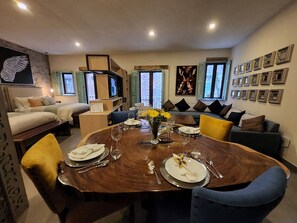 A dining area with a wooden table set for four, surrounded by sofas and chairs.