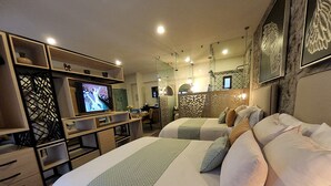 A hotel room with two beds, a TV, a desk, and a dining area.