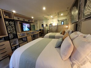 A hotel room with two beds, a TV, a desk, and a dining area.