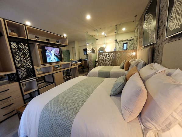 Ein Hotelzimmer mit zwei Betten, einem Fernseher, einem Schreibtisch und einem Essbereich.