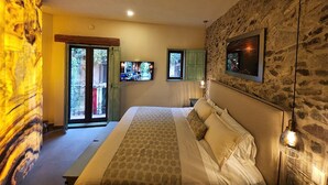 A bedroom with a bed, a television, and a stone wall.