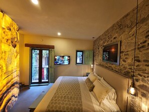 A bedroom with a bed, a television, and a stone wall.