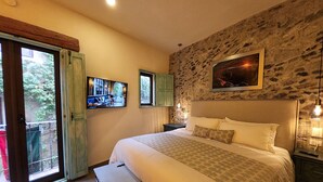 A bedroom with a large bed, a stone wall, a painting, and a window with a view.